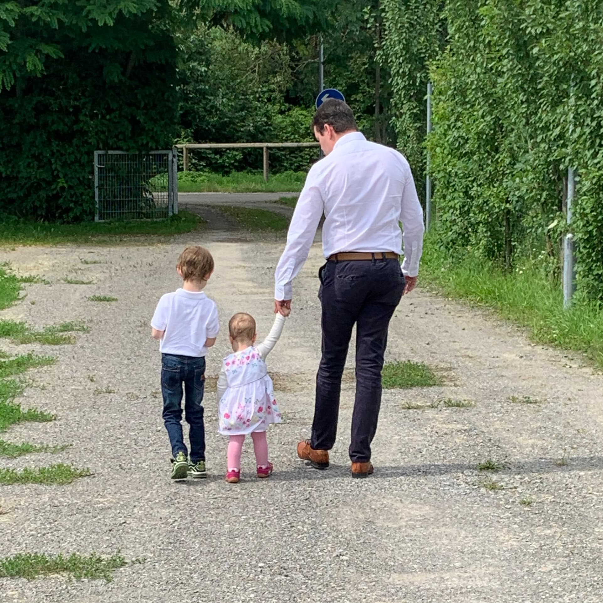 Ein Mann geht mit zwei kleinen Kindern einen Feldweg entlang, das jüngere Kind hält seine Hand